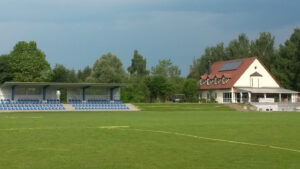 Moderne Fußballschule Fotografiebild mit Tribüne, Spielfeld und Wohnhaus, ideal für Fußballferien und Nachwuchsförderung im sportlichen Umfeld, bei schönem Wetter.