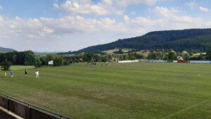 Freundliches Fußballtraining bei Hans Dorfner Fußballschule im ländlichen Gelände. Spieler üben auf dem grünen Rasen, um ihre Fußballfähigkeiten zu verbessern. Das beeindruckende Naturpanorama im Hintergrund ergänzt die sportliche Atmosphäre.